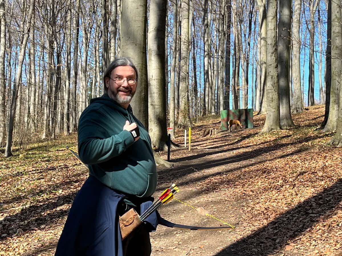 Michael Smetana im Wald, in grüner Kleidung und mit Pfeilen im Köcher an der Hüfte